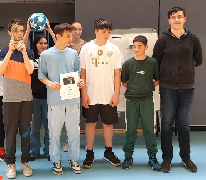 Schulmeisterschaft 7./8. Klasse Basketball am 28.04.2025 - 7 Schüler auf dem Bild, ein Schüler hält den Ball hoch ein anderer Schüler hält die Urkunde in die Kamera